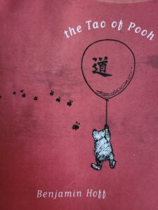 red mottled background with black and white pooh bear flying from a ballon. little black bees scatter to the left, inside the ballon is a Chinese symbol and above it the words "The Tao of Pooh"