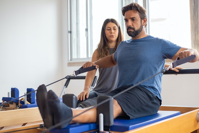 Image of man with prosthetic leg on pilates reformer with teacher