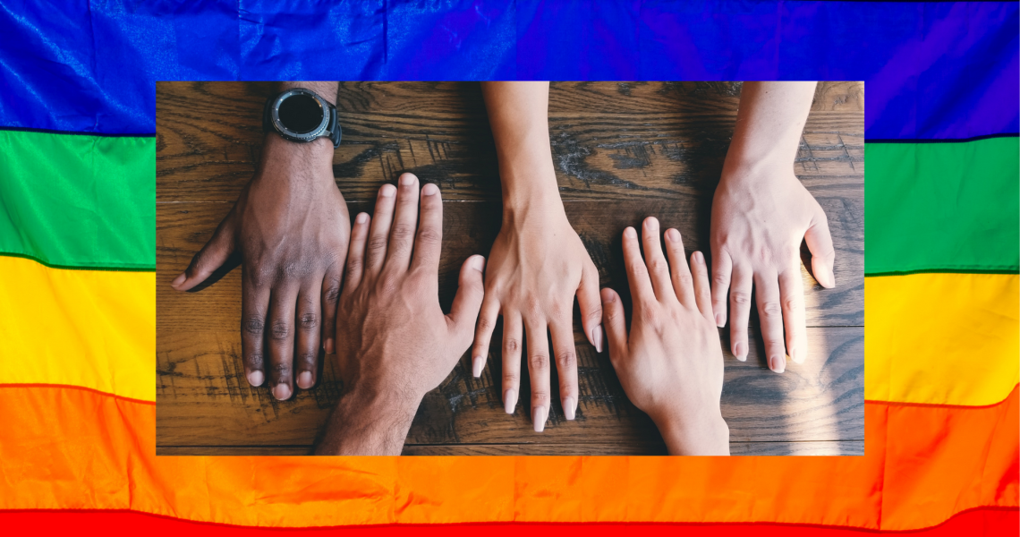 pride flag background with five human hands of varying skin color resting beside each other on a table