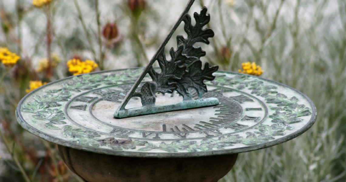 old fashioned sundial with background of yellow flowers and greenery